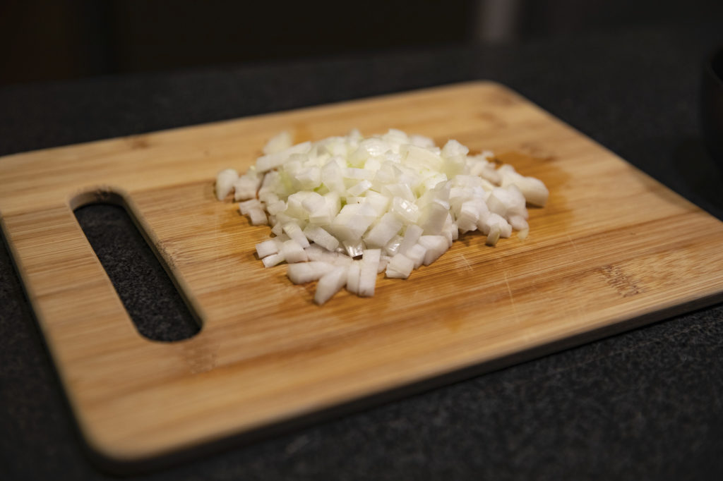 A diced onion sitting on a bamboo cutting board.